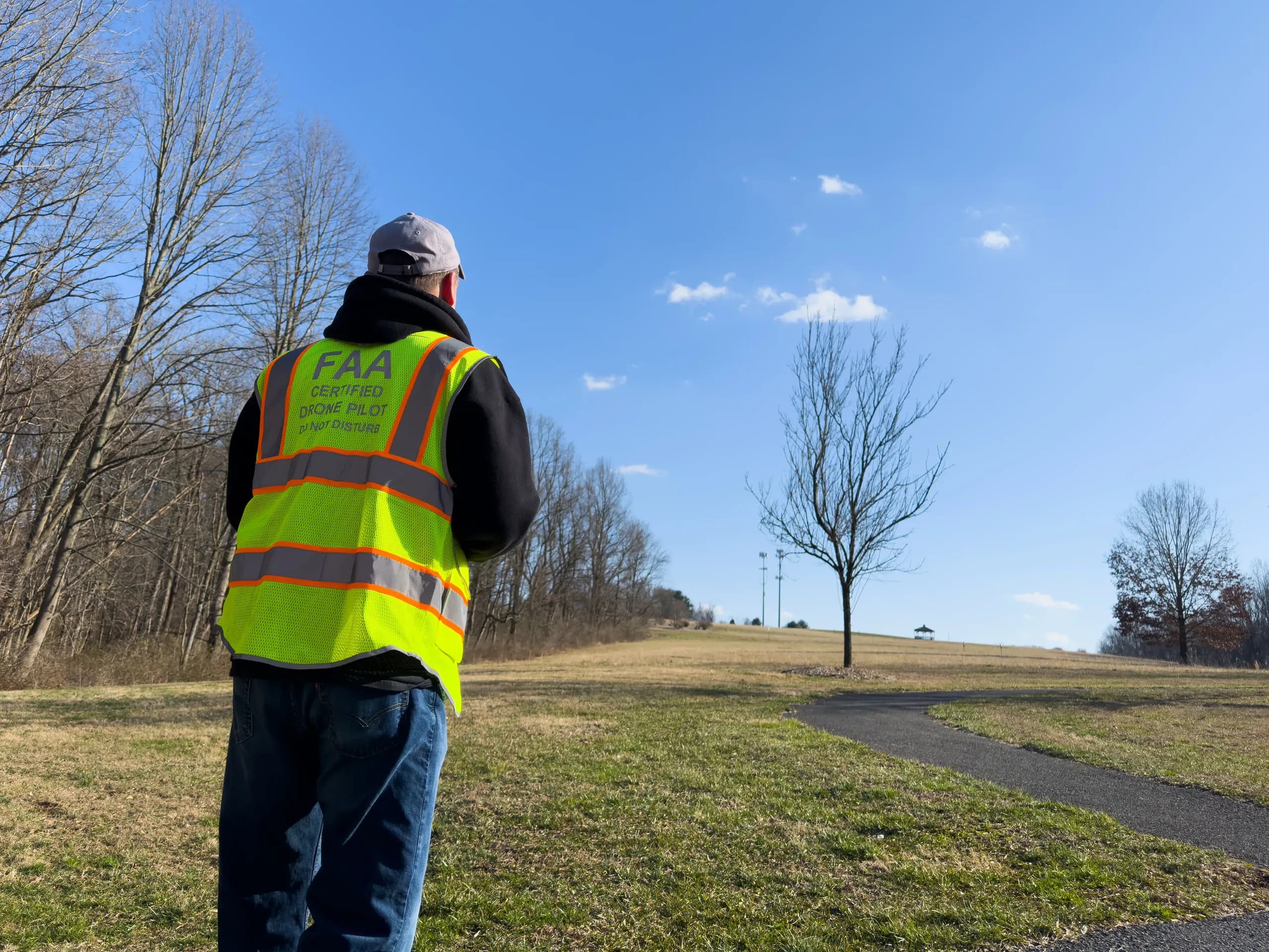 The ZigZag Aerial pilot on site at Crossan Park in Landenberg, Pennsylvania, in an FAA certified drone pilot vest, facing the field he is about to fly
